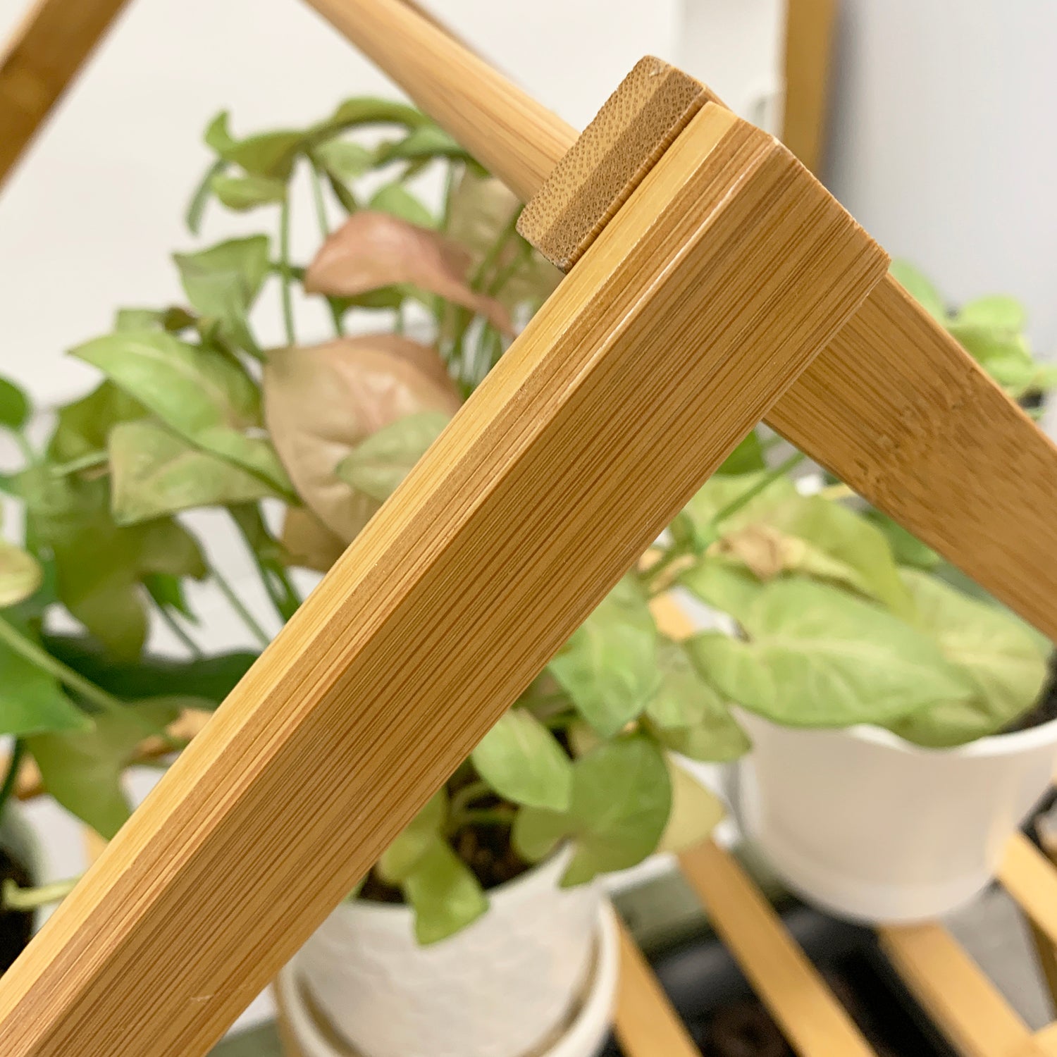 A close-up of a bamboo indoor plant stand with multiple tiers, featuring wooden slats and supporting several potted plants.